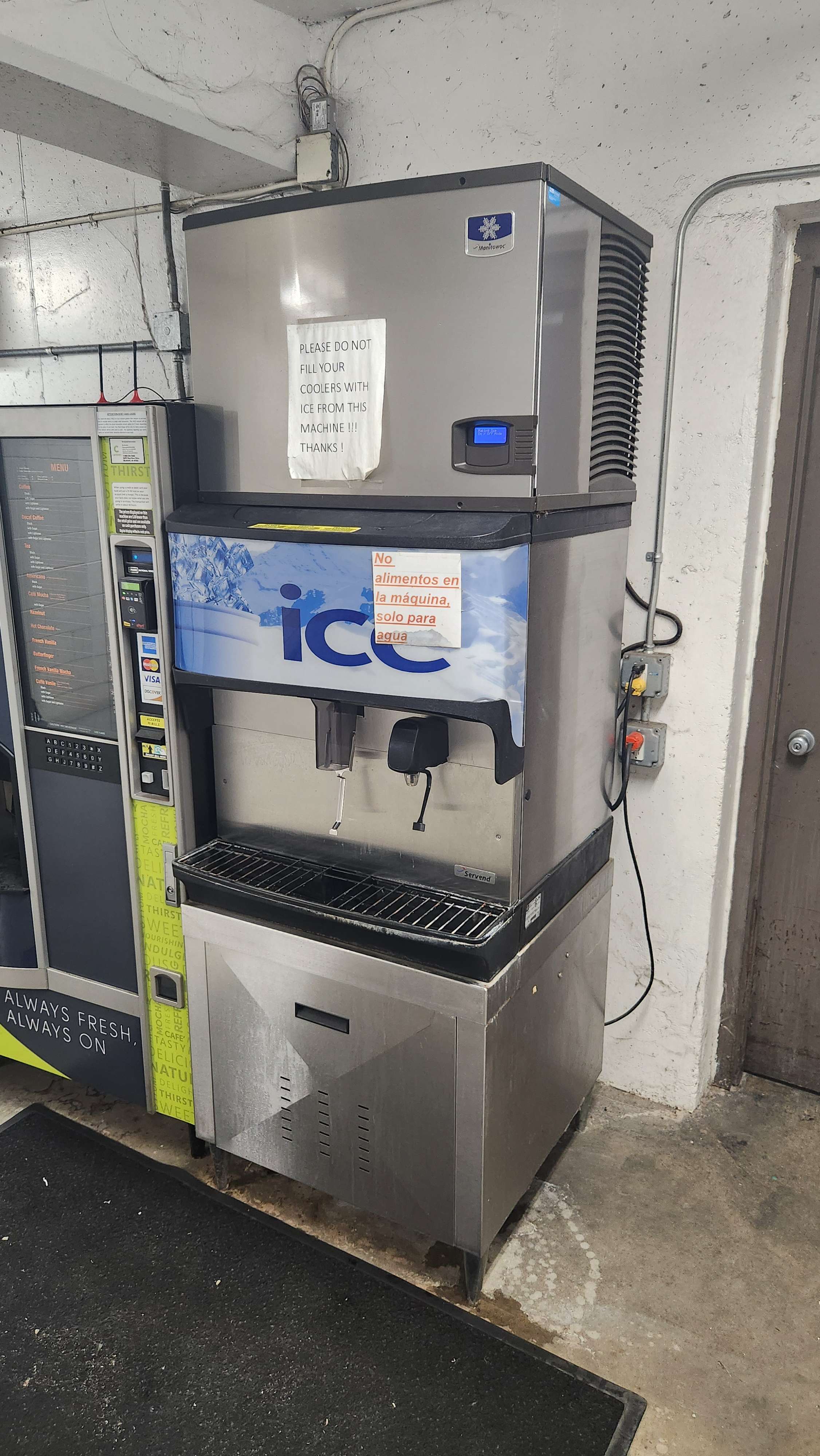 Stainless steel ice machine with warning signs in English and Spanish